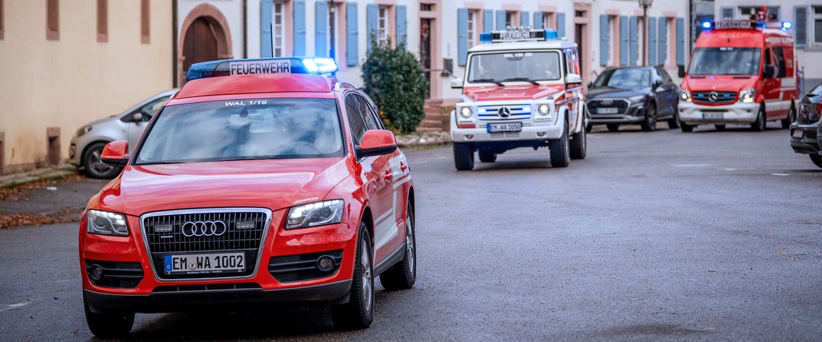 Feuerwehrfahrzeuge unterwegs in einer Stadtstraße, mit Blaulicht und Einsatzfahrzeugen im Vordergrund