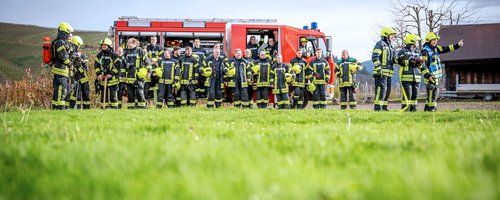 Gruppenfoto der Feuerwehrleute vor einem Feuerwehrauto auf einer Wiese