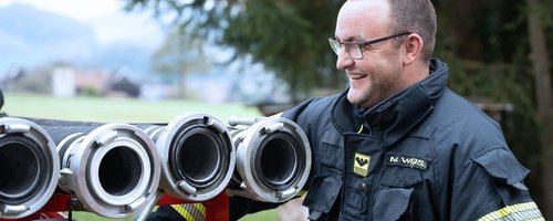 Feuerwehrmann bereitet sich auf den Einsatz vor, mit Saugschläuche im Vordergrund.